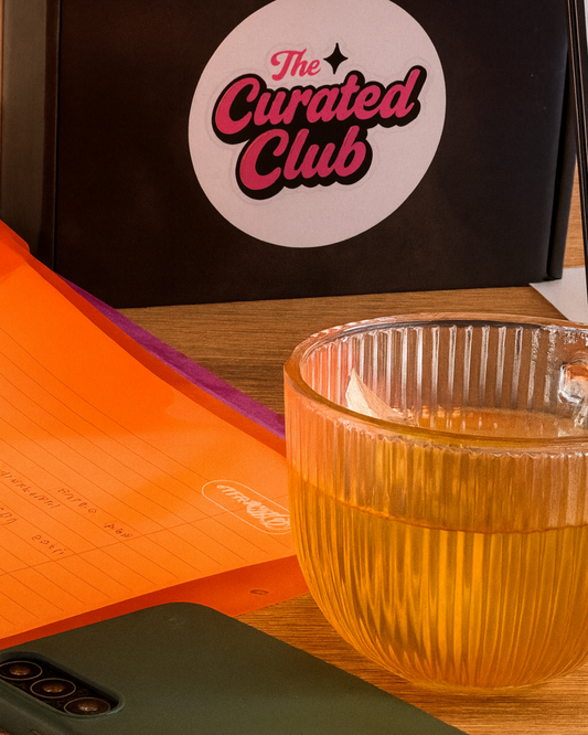 A cup of tea beside a Curated Club subscription box, files and laptop in the background