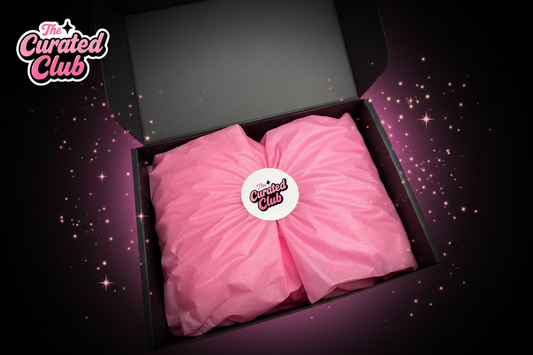 The Curated Club subscription box open with pink tissue paper and branded sticker, with sparkles on a dark background